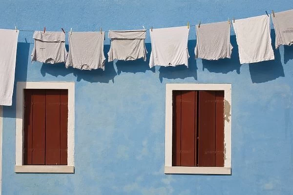 Italy, Burano. Hanging laundry and windows along blue wall