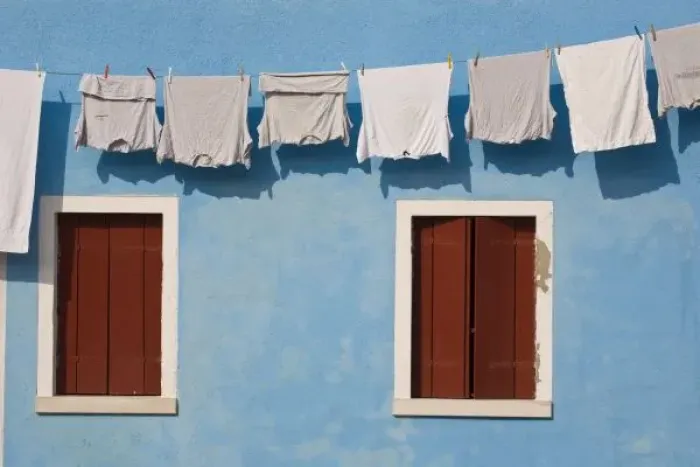 Framed Print : Italy, Burano. Hanging laundry and windows along blue wall