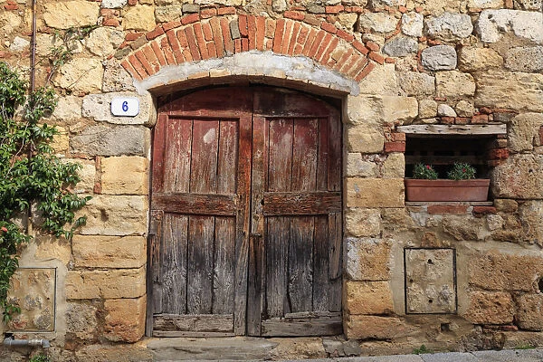 Italy, Monteriggioni. Stone wall, wooden door with planted geraniums