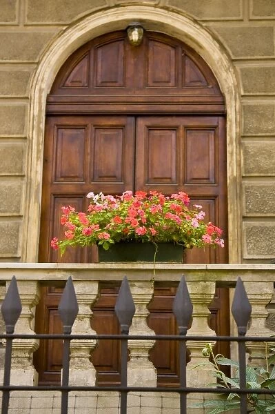 Italy, Parma. A pot of pink flowers decorates the railing in front of a wooden door