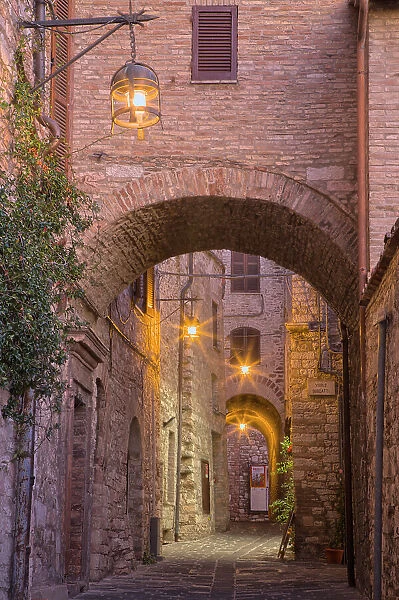 Italy, Umbria, Assisi. Alleyway with arches and lanterns in the evening