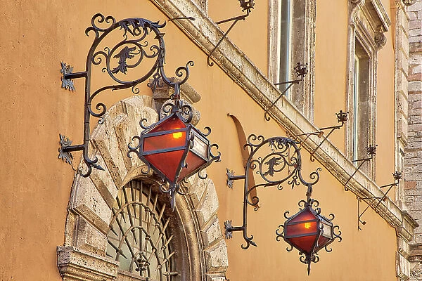 Italy, Umbria, Assisi. Wrought iron dragon lights on a wall above an entrance