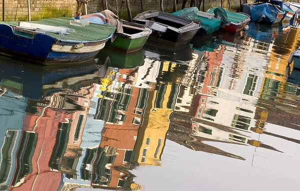 Italy, Venice, Burano. Row of boats and colorful houses reflect in canal water. Credit as