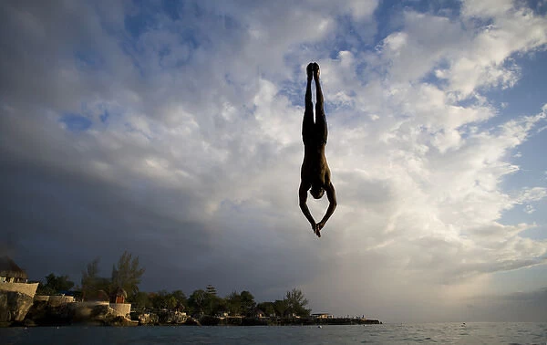 Jamaica, Negril, Silhouette of young man leaping from from cliff above Pirates Cave