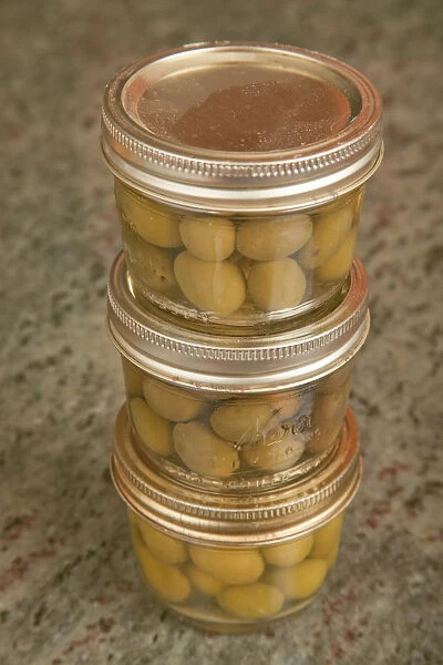 Three jars of home canned olives on a granite countertop in a kitchen