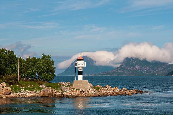 A lighthouse perches on a rocky promontory and reflects on Holandsfjorden. Svartisen, Norway