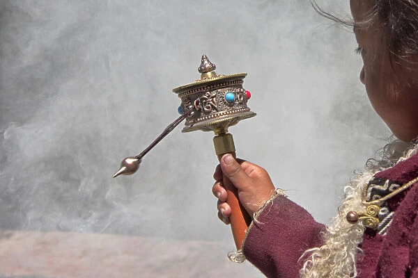 Little Tibetan girl praying with prayer wheel and smoke from incense in Drepung Monastery