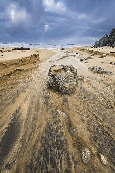 Low angle of a stream flowing around a rock heading into the ocean with stormy skies