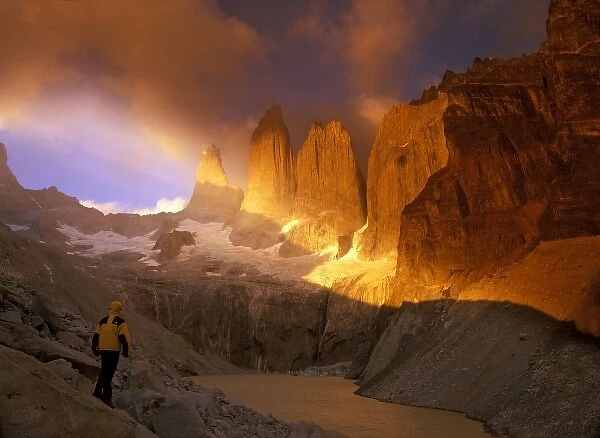 Man in yellow jacket watches as clouds swirl around Cerro del Torres in Patagonia, Chile