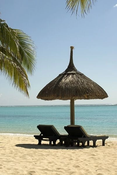 Mauritius. Idyllic beach scene with umbrella, chairs and palm fronds