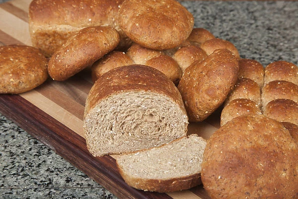 Multigrain rolls, buns and loaf with a slice cut off, on bread board