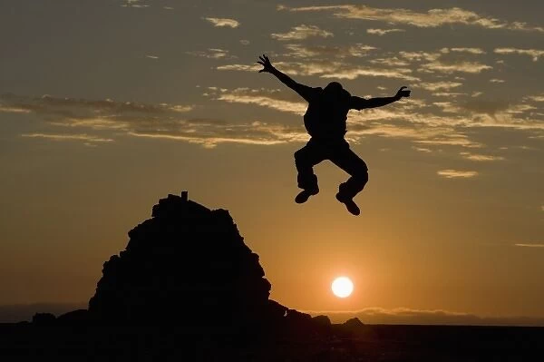 Namibia, Namib Naukluft National Park, Silhouette of man leaping from rock cairn