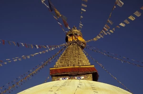 Nepal, Kathmandu. Under prayer flags, watchful eyes of Buddha gaze from Bodhnath Stupa, c