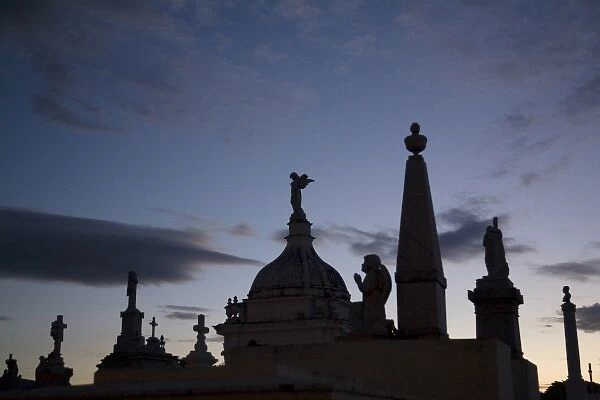 Nicaragua, Granada. Silhouettes of crosses and angels on top of graves in cemetery at sunset