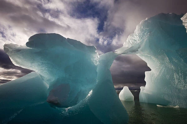 Norway, Svalbard, Spitsbergen Island, Morning sun lights melting arched iceberg floating