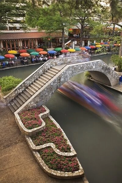 Outdoor cafe along River Walk and boat in motion passing under bridge over San Antonio River