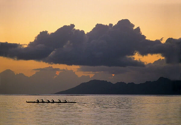 An outrigger canoe team practices off the coast of the island of Tahiti as the sun
