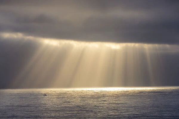 Rays emit from the clouds over the Pacific Ocean as fishing boat passes by near Santa Cruz
