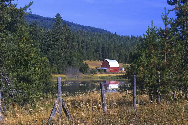 A red barn in relected in a lake near Hayden Lake, Idaho. The old fence in the foreground