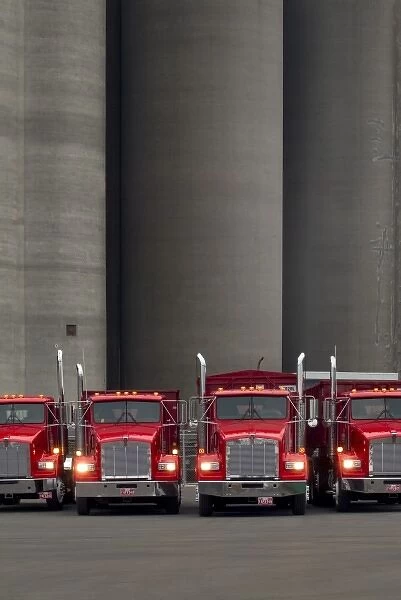 Four red trucks with lights turned on lined up in front of tall concrete silos in