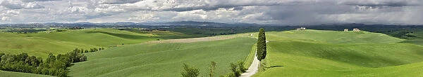 Road winding through agricultural region of Tuscany with storm clouds, Italy