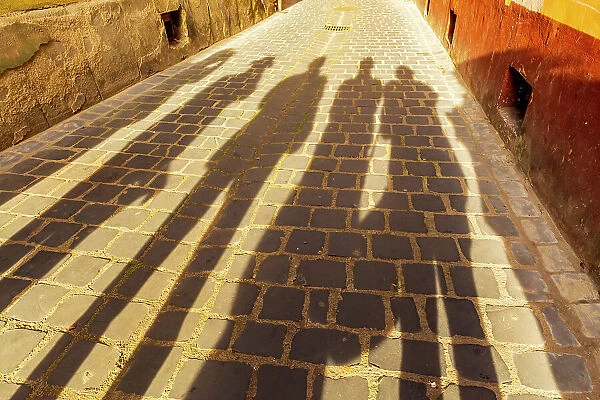 Romania, Brasov. Shadowed figures in silhouette on street cobblestone
