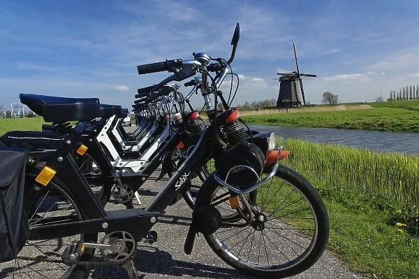 Row of bicycles along on dike along canal, and distant windmill, Holland, Netherlands