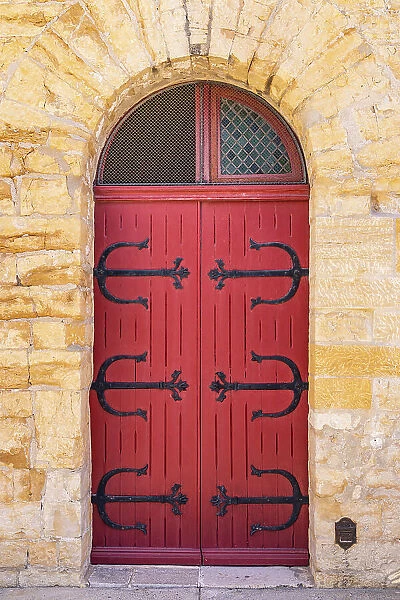 Saintes-Maries-de-la-Mer, Bouches-du-Rhone, Provence-Alpes-Cote d'Azur, France. Red door with metal hinges in a stone building
