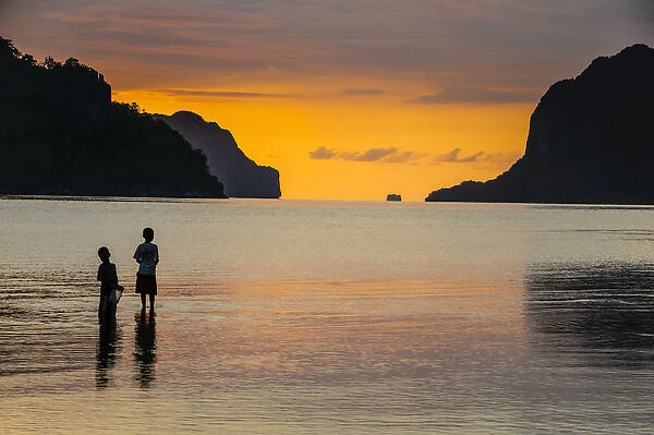 Silhouette of boys fishing at sunset in the bay of El Nido, Bacuit Archipelago, Palawan