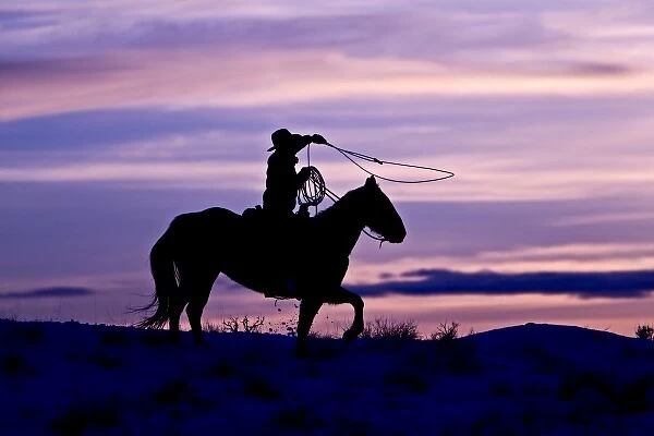 A silhouette of a cowboy on horses with the winter sky on The Hideout Ranch in Shell Wyoming