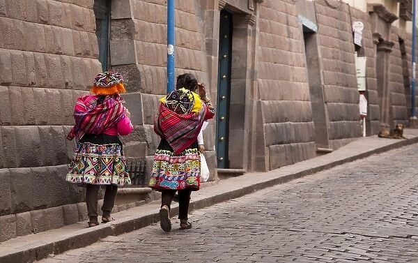 South America, Peru, Cuzco. Two women in traditional dress walk along the stone street
