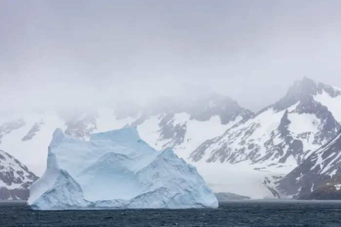 Framed Print : South Georgia Island. Large iceberg floats past mountains