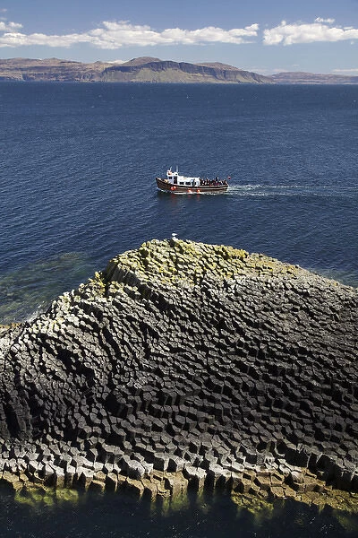Staffa tour boat and polygonal basalt, Am Buachaille rocks, Staffa, off Isle of Mull (in distance)