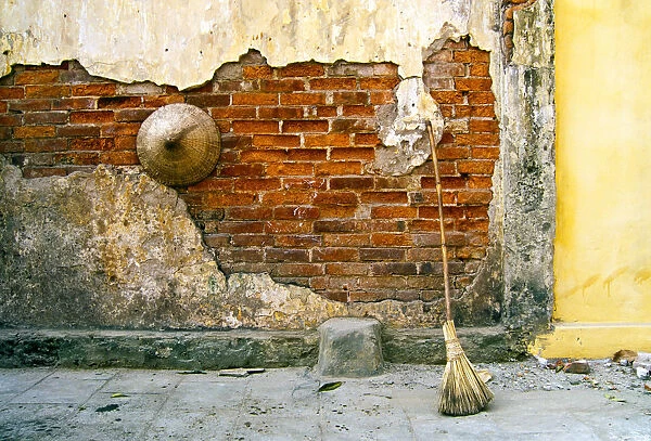Still-life of a hat and broom against a weathered wall in Vietnam