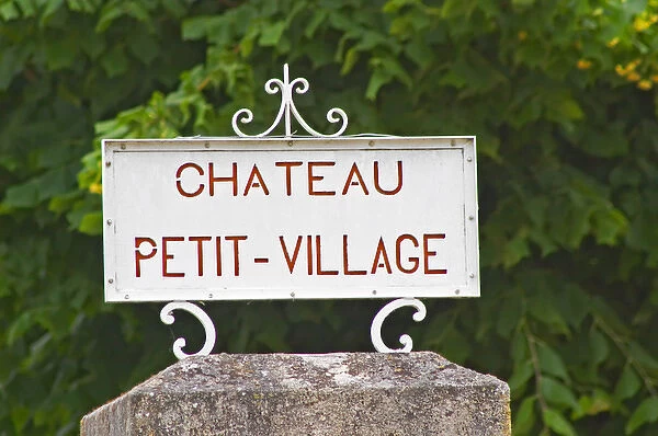 A stone gate post and a white sign saying Chateau Petit Village, detail Pomerol