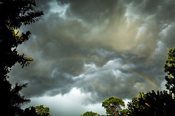 Storm clouds approach in this photograph while a rainbow is illuminated by sunrays