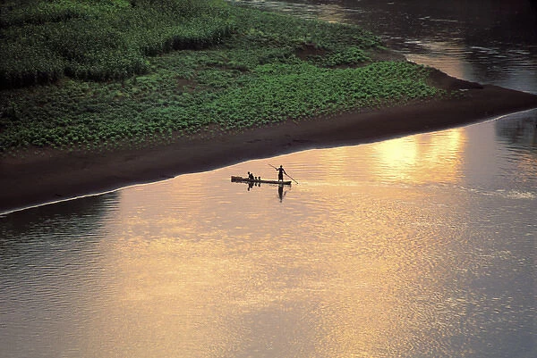 The sun sets on some Karo men piloting a dugout raft across the Omo River, near their
