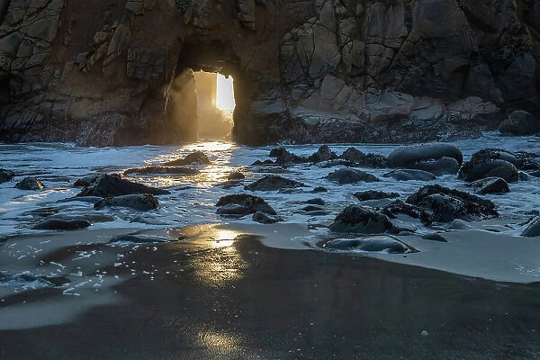 Sun shines through a tunnel in a sea cliff in the Big Sur area
