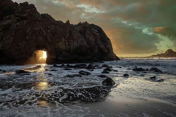 Sunset shines through a tunnel in this sea rock at Big Sur