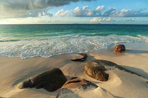 Surf surging towards boulders buried in sand on a tropical beach. Anse Victorin Beach, Fregate Island, Seychelles