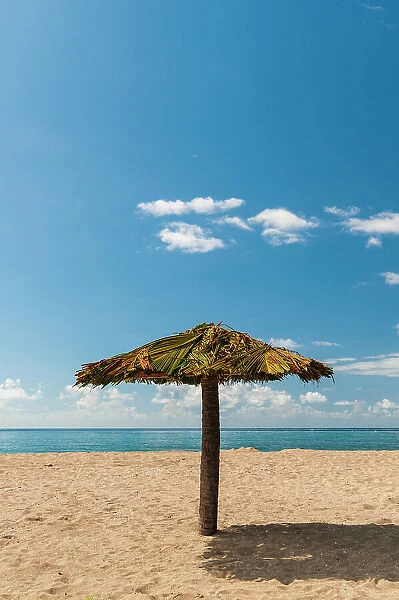 A tiki umbrella on a palm tree trunk on Pinney's white sand beach. Nevis Island, West Indies