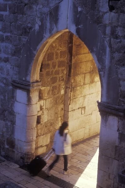 A tourist briskly walks through the inner gate at the Pile Gate entrance to Old Town Dubrovnik