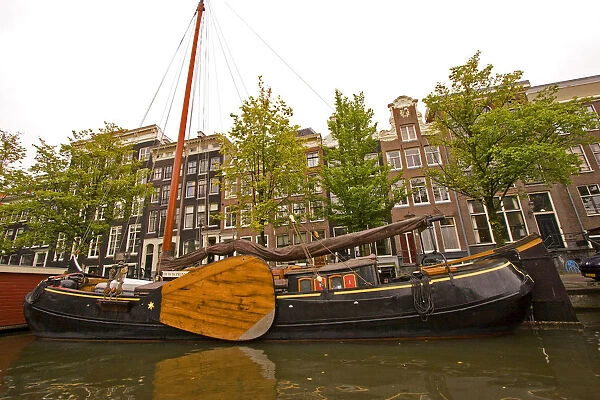 Unusual sail boat with large wooden paddle on a canal lined with homes
