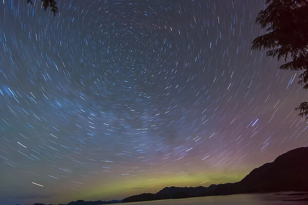 US, AK, Ketchikan. Northern Lights glow on horizon with star trails rotating around North Star