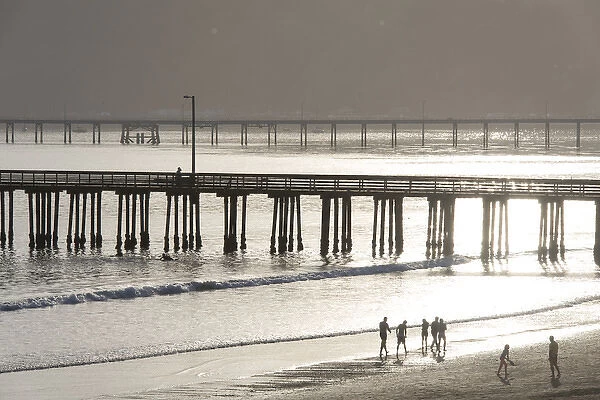 US, CA, Avila Beach. Silhouetted beach walkers approach pier end of day