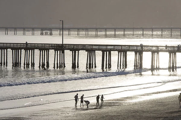US, CA, Avila Beach. Silhouetted beach walkers approach pier end of day