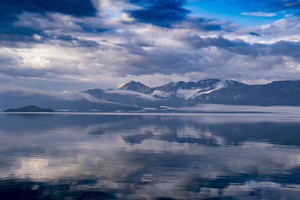 Usa, Alaska. Clouds and mountains reflect in the calm waters of Endicott Arm
