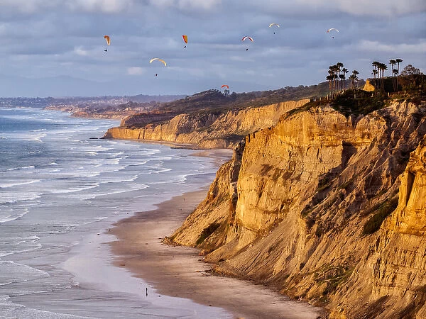 USA, California, La Jolla, Paragliders float over Blacks Beach in late afternoon