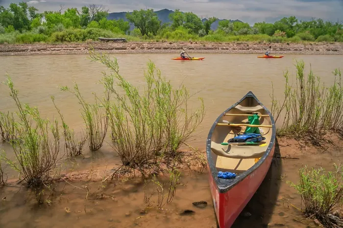 Framed Print : USA, New Mexico, Rio Grande River. Empty canoe on riverbank and kayakers on river