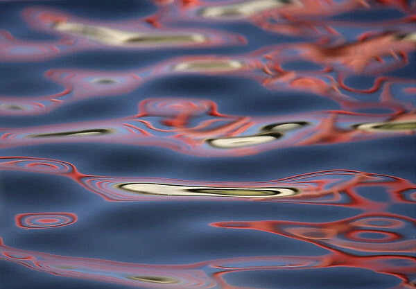 USA, New Mexico, Socorro. Bridge reflections create abstract swirling red patterns in water